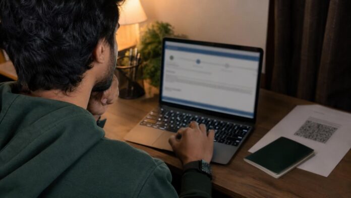 Applicant checking his Saudi visa status online by passport number on a laptop, with passport and printed e-visa